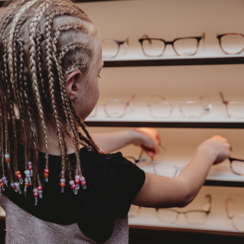 Enfant avec des tresses qui prend une lunette dans un présentoir 