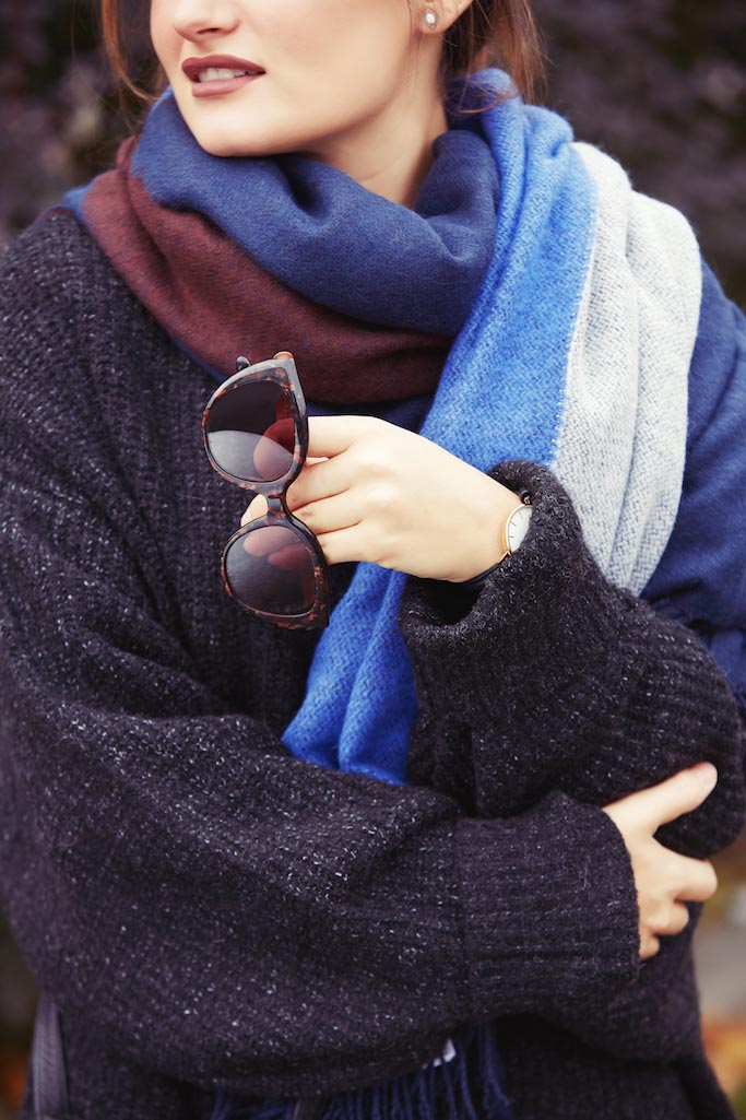 Femme avec un grand foulard bleu tenant ses lunettes de soleil