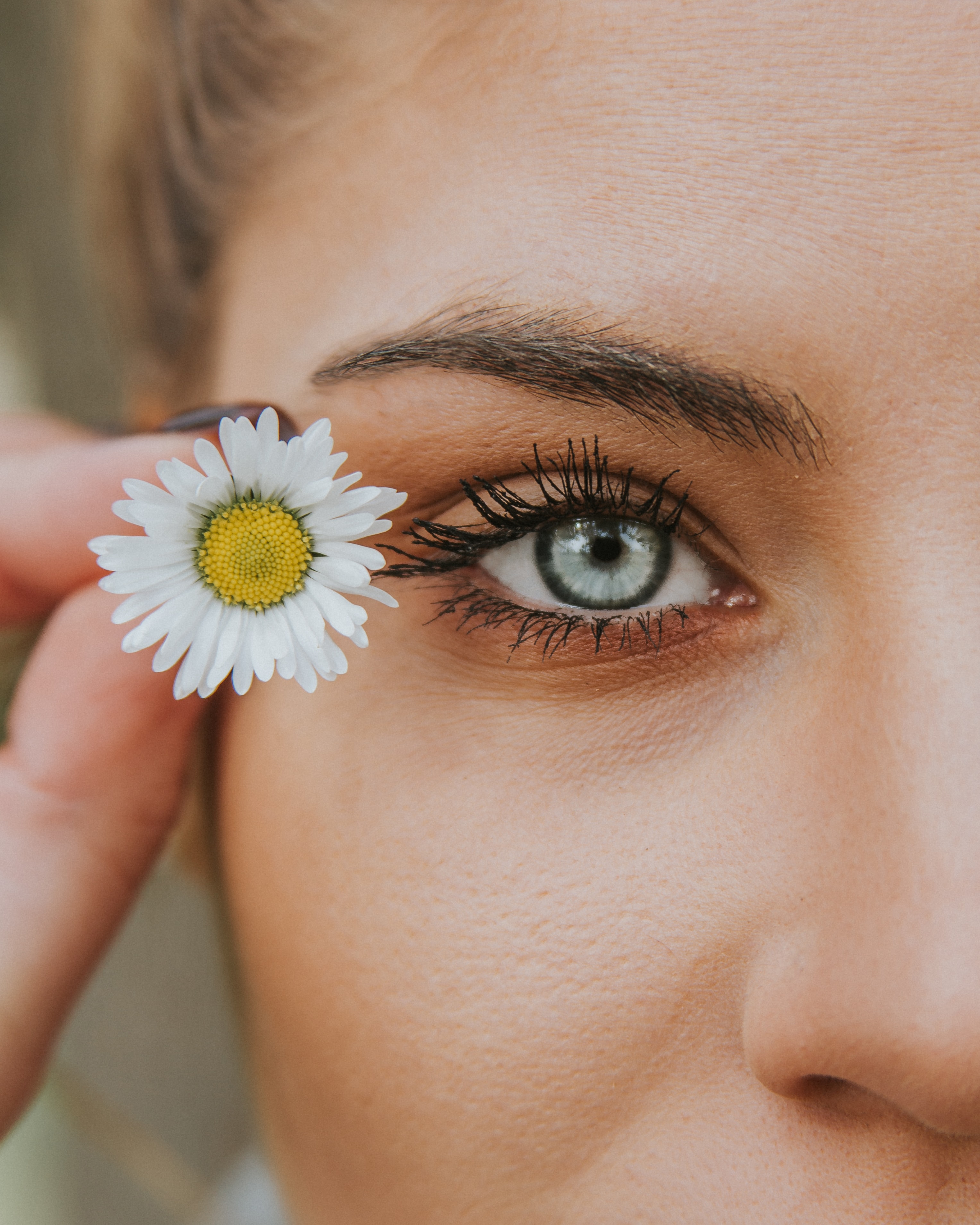 Woman holding a daisy next to her blue eye