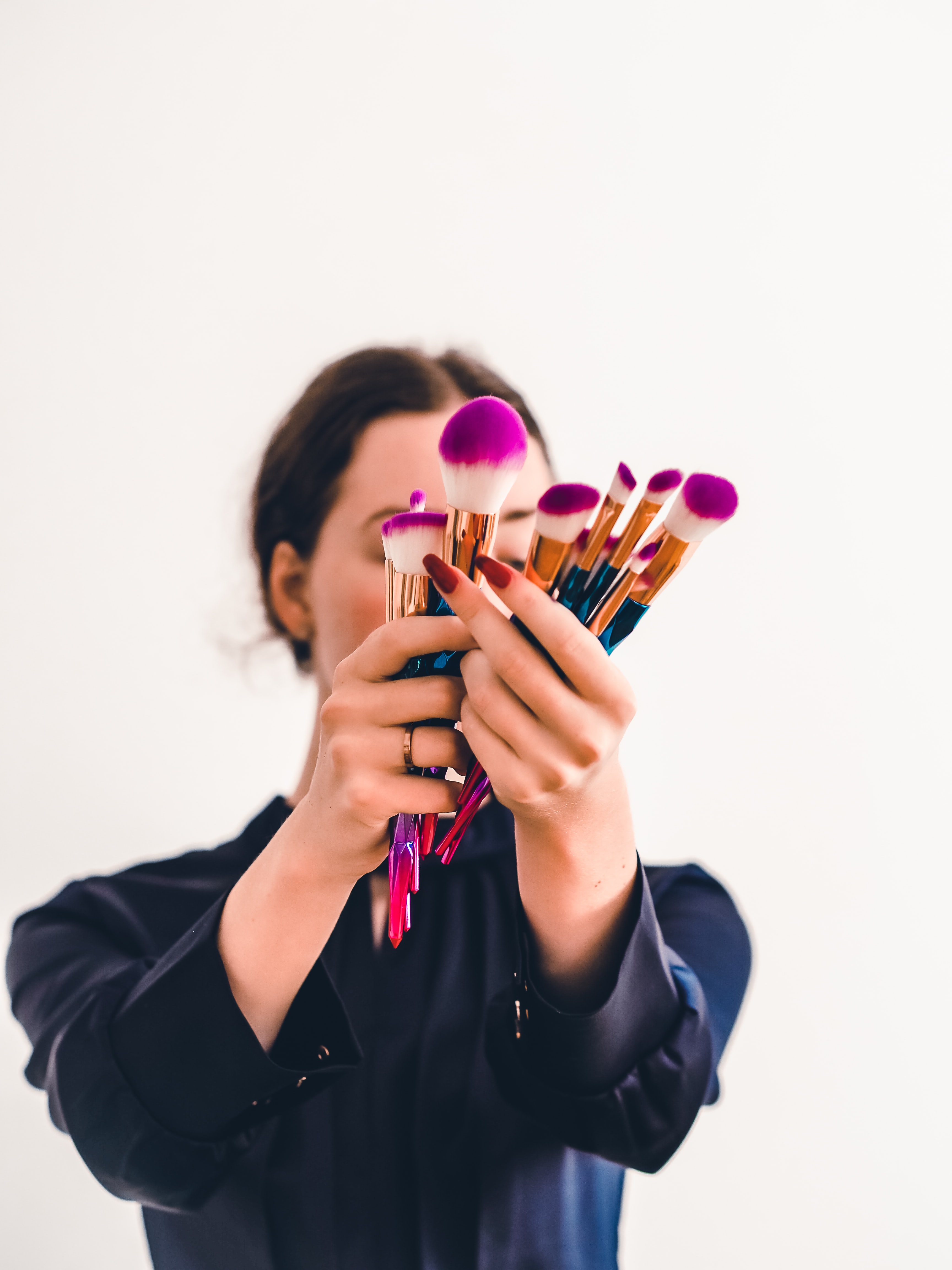 Femme tenant plusieurs pinceaux à maquillage devant son visage