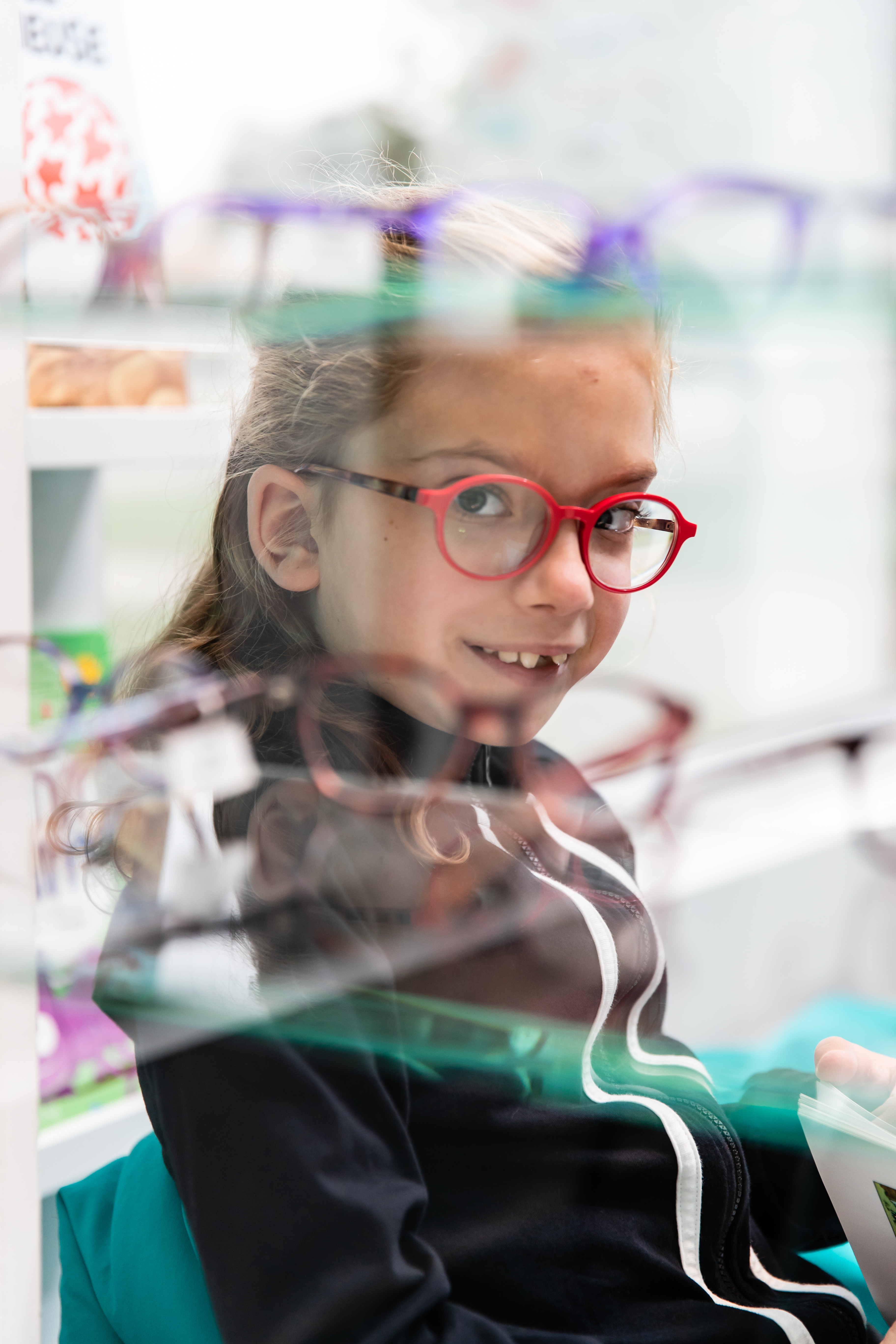  girl with red glasses looking through a spectacle display rack